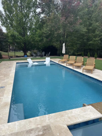 Backyard pool with chairs and trees.