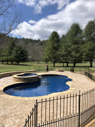 Fenced outdoor pool with trees and hill view.