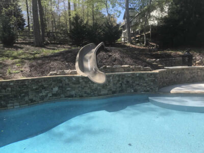 Curved pool slide with stone wall backdrop.