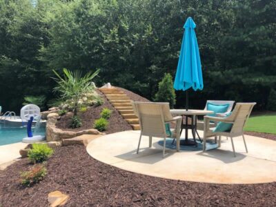 Outdoor patio set beside swimming pool and trees.