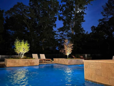 Night swimming pool with illuminated trees and chairs.