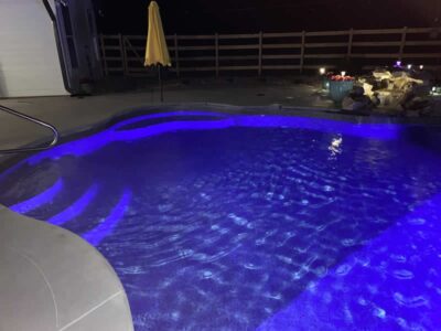 Illuminated backyard pool at night with umbrella.