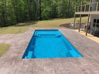 Backyard pool with wooden deck and surrounding trees.