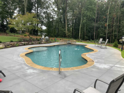 Backyard pool surrounded by trees and chairs.