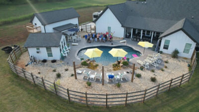 Drone view of house with pool and people outside.