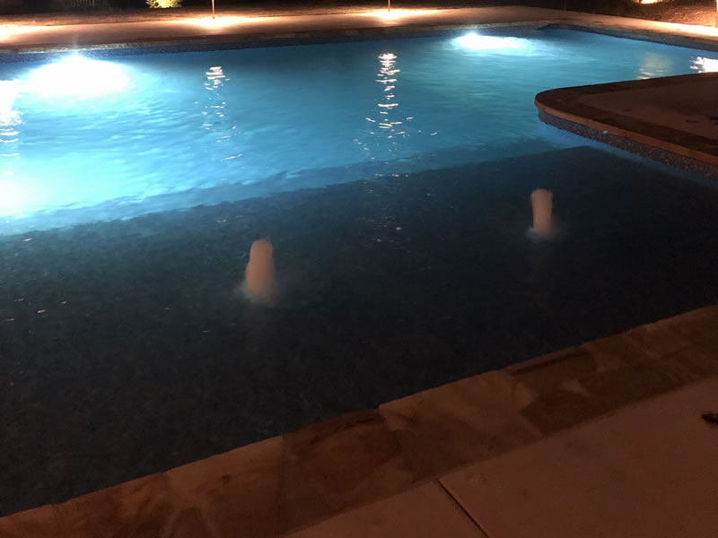 Illuminated swimming pool at night with fountains