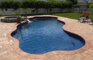 Curved backyard swimming pool with paver patio and spa