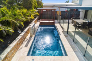 Narrow backyard pool beside tropical landscaping and patio dining