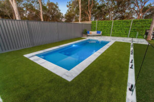 Modern backyard pool with turf, fencing, and lounge seating
